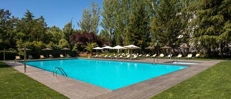 A rectangular swimming pool with a wooden deck surrounding it, surrounded by green grass and trees.