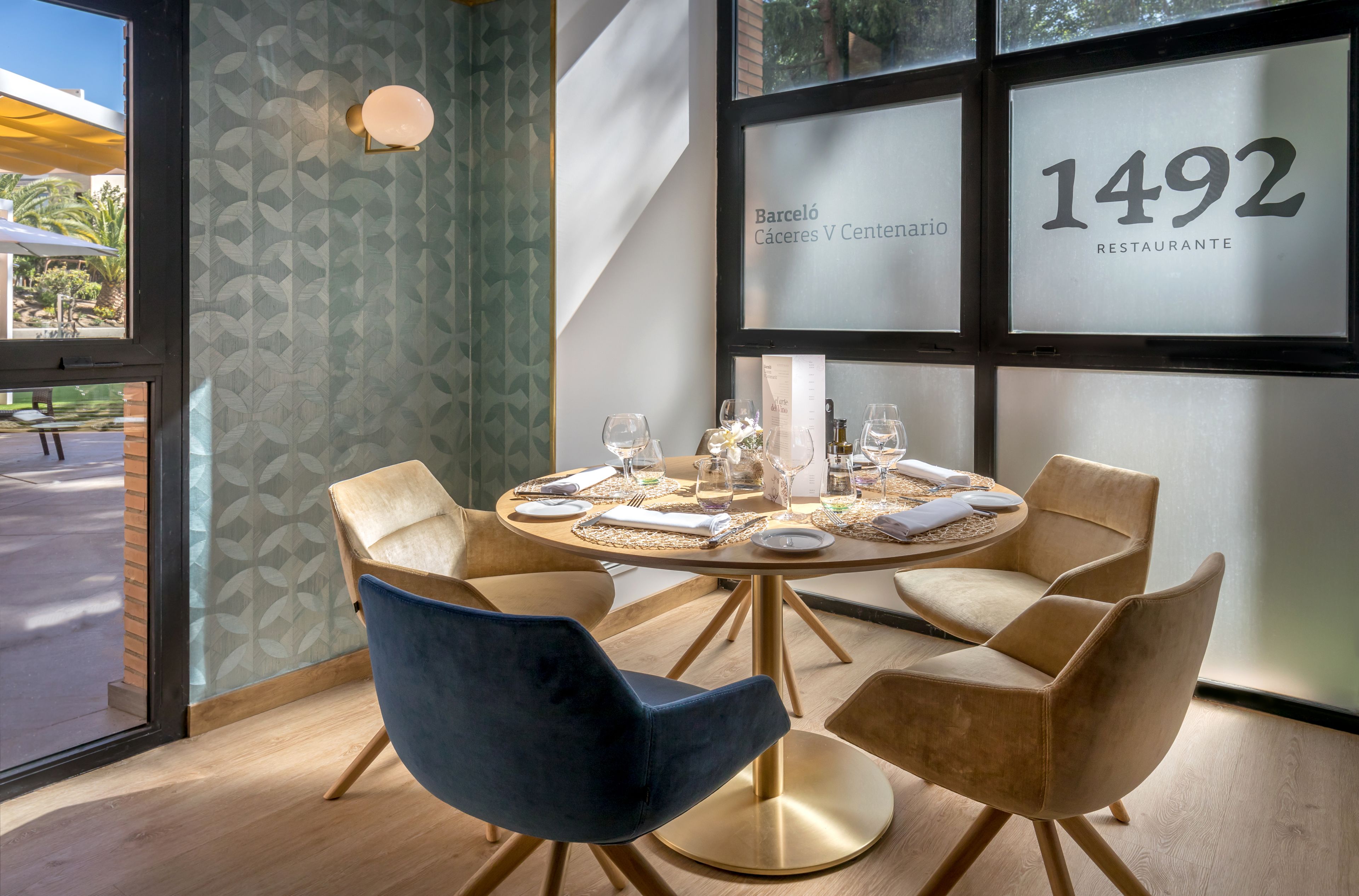 Un coin repas avec une table ronde dressée pour quatre personnes, entourée de quatre chaises, et une grande fenêtre sur laquelle on peut voir le numéro 1492.