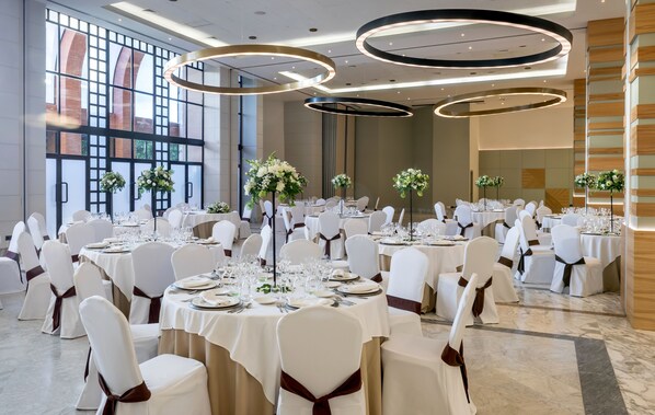 A banquet hall with round tables, white chairs, and floral centerpieces. - Barceló Cáceres V Centenario (Cáceres)