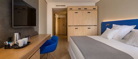 Una habitación de hotel con una cama, un escritorio con cafetera, una silla y un televisor montado en la pared.