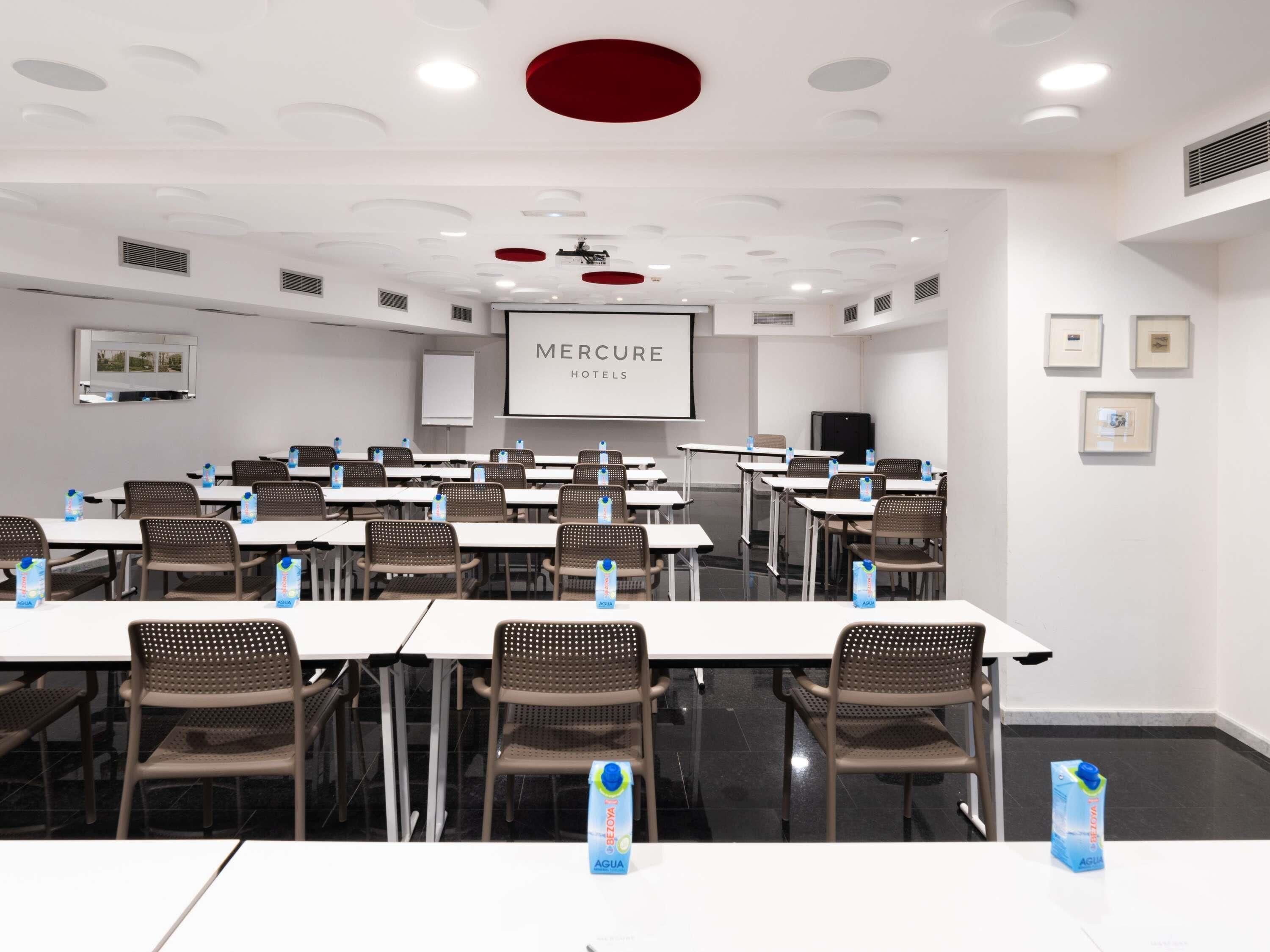 A conference room with tables, chairs, a projector screen, and a whiteboard.