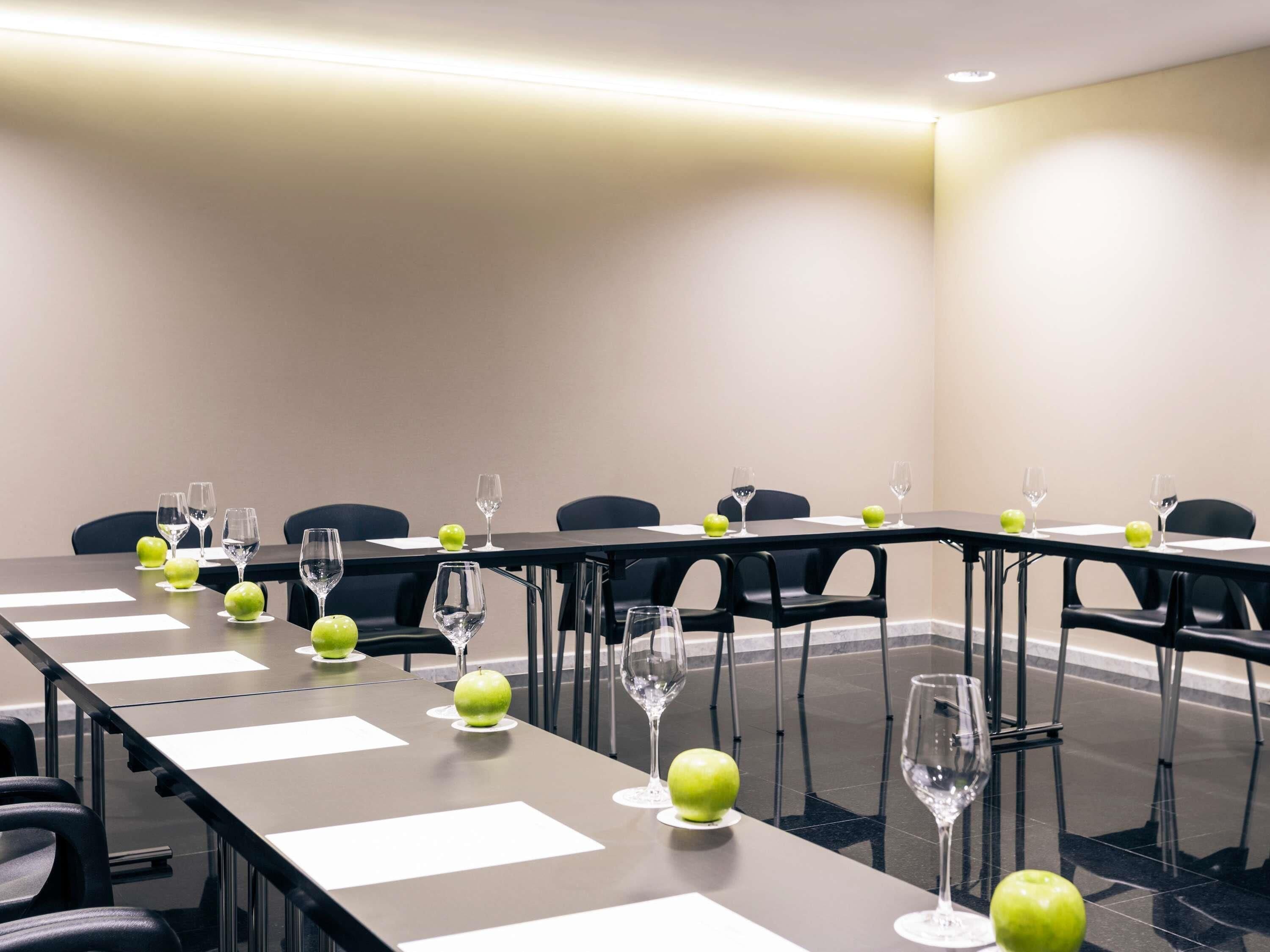 Un salón de conferencias con una larga mesa, sillas y vasos con manzanas.