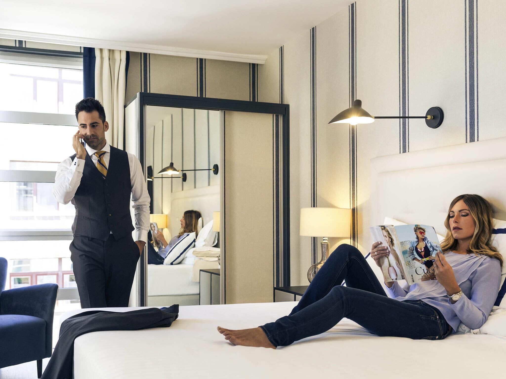 Una habitación de hotel con cama, zona de estar, espejo y ventana.