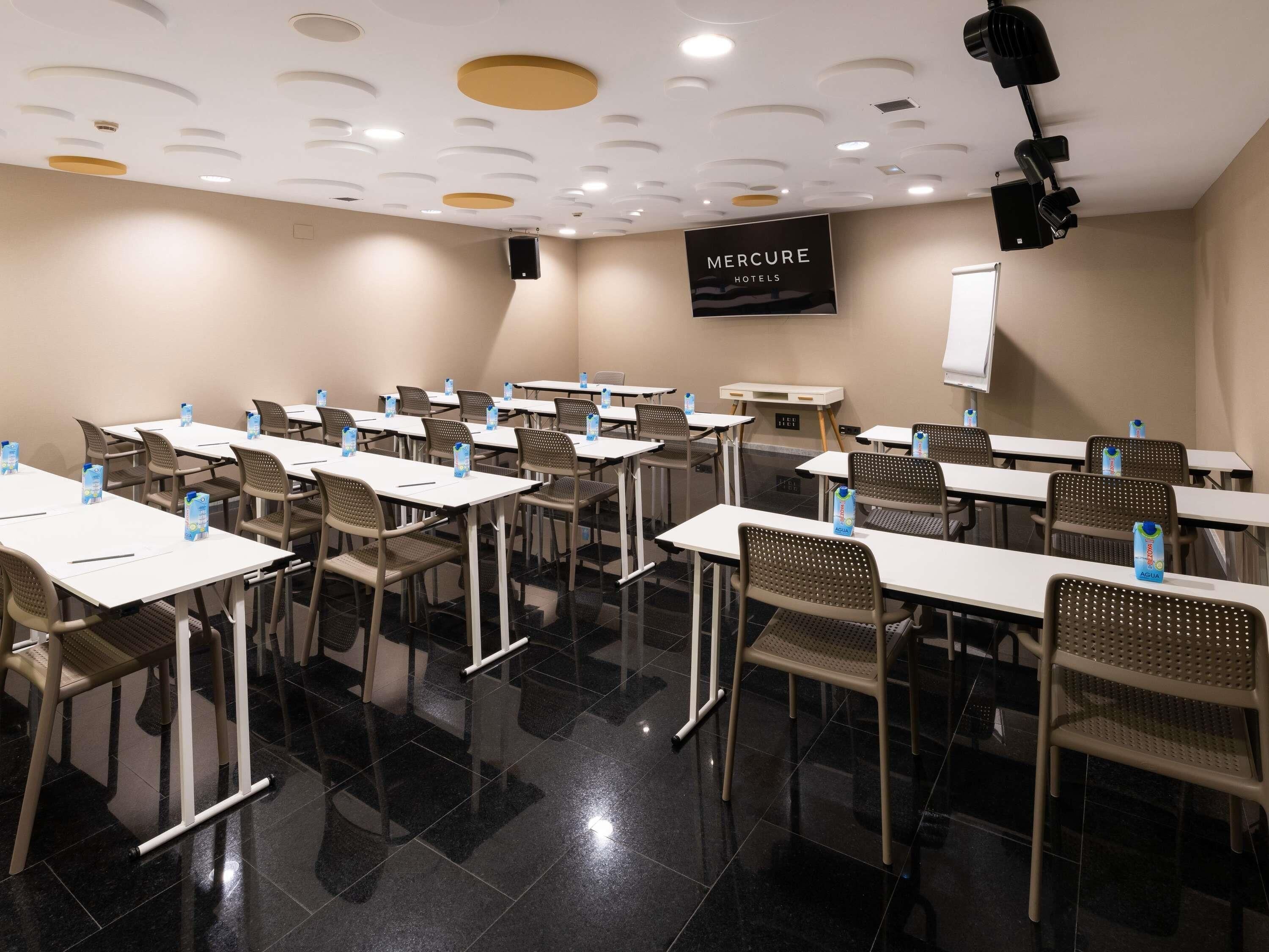 Un salón de conferencias con mesas y sillas, una pizarra y un cartel de Mercure Hotels.