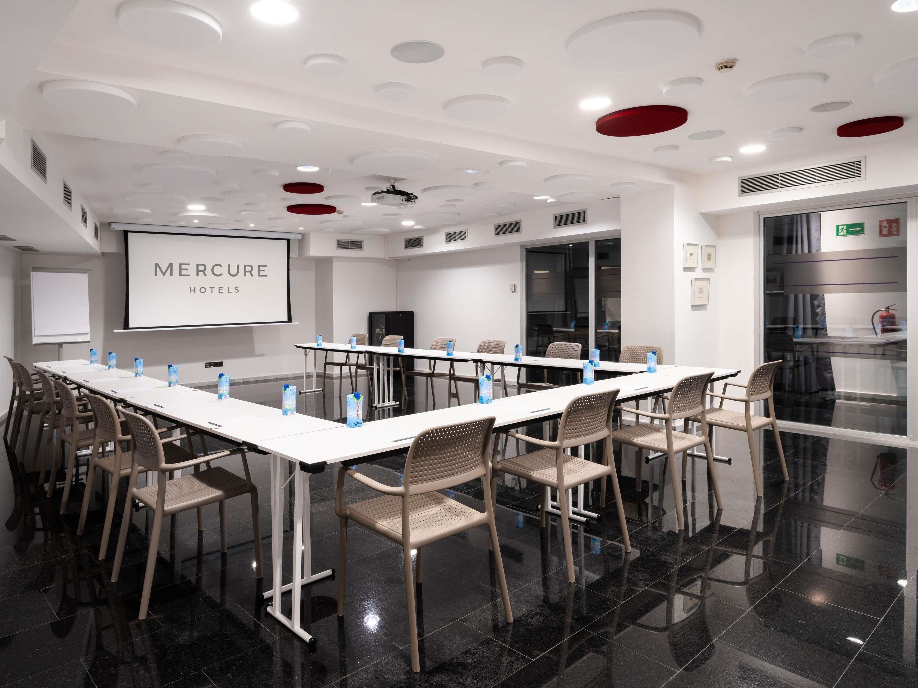 A conference room with a long table, chairs, a projector screen, and a whiteboard.