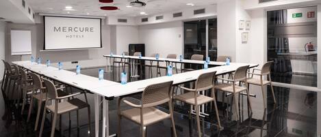 A conference room with a long table, chairs, a projector screen, and a whiteboard.