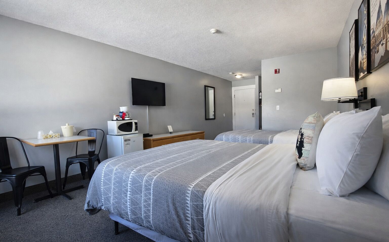 A hotel room with two beds, a desk with a microwave, a chair, and a TV on the wall.