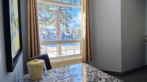 Una habitación con un ventanal grande, una mesa con mantel estampado y una silla.