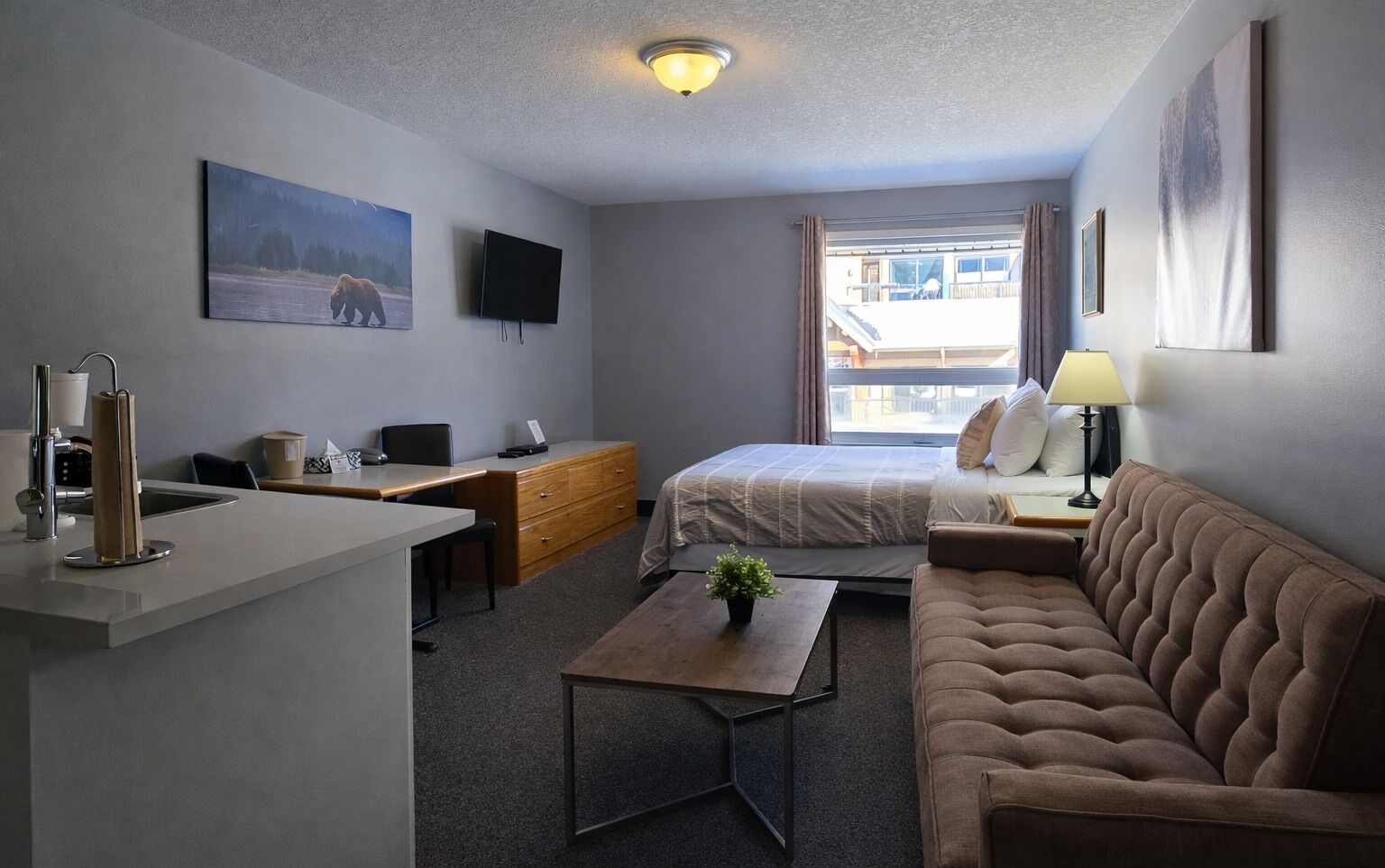 A compact hotel room with a bed, a sofa, a desk, and a television.