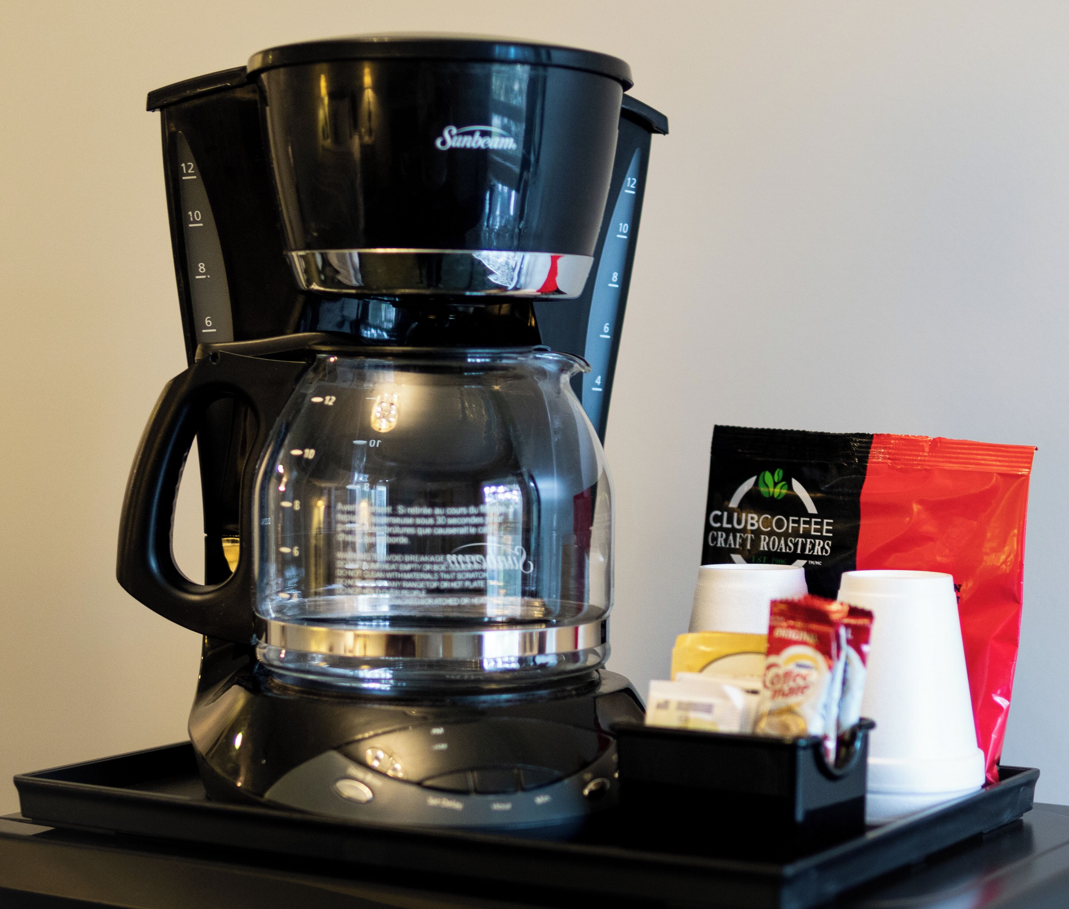 Une machine à café avec une verseuse en verre, une dosette de café et une tasse à café, le tout posé sur un plateau.