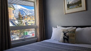 Un dormitorio con un ventanal grande, una cama con ropa blanca y vistas a la montaña.