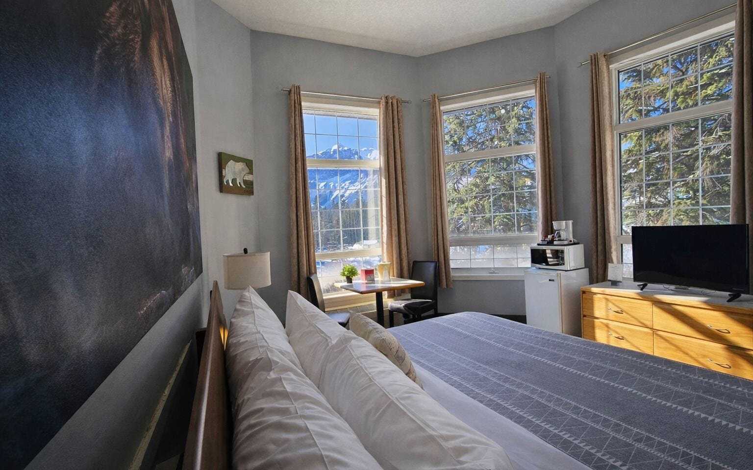 Una habitación de hotel con cama, escritorio, televisión y ventana con cortinas.