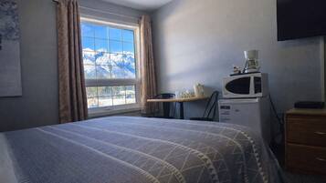 Habitación de hotel con cama, ventana con cortinas, escritorio con silla, microondas y televisor en la pared.