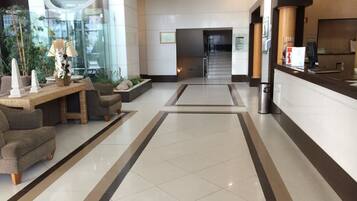 A spacious lobby with a reception desk, seating area, and a glass wall with plants.