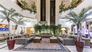 Un hall d’entrée spacieux avec un espace salon central, de grands pots de plantes et un plafond haut laissant entrer la lumière naturelle.