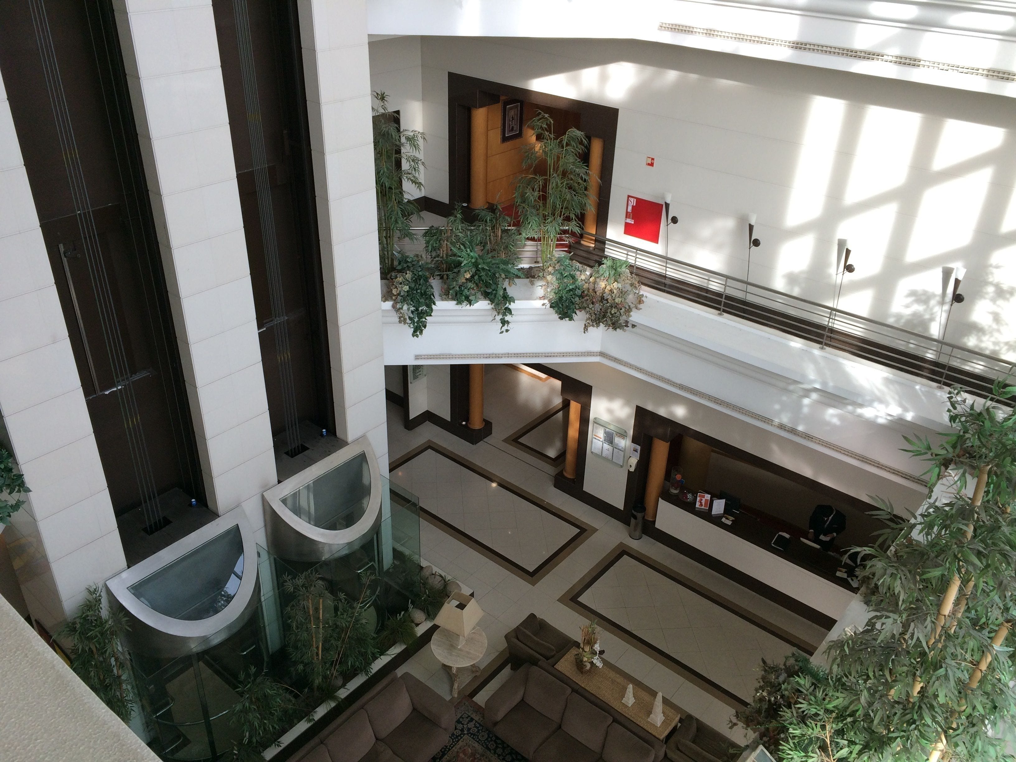 A multi-level atrium with a central staircase, glass railings, and indoor plants.