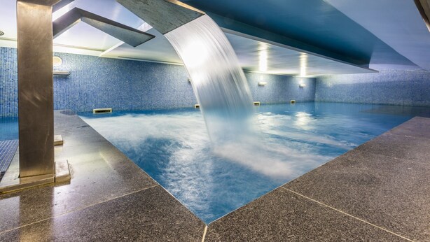 Une piscine intérieure au design moderne, dotée d’un élément aquatique original et d’un mur recouvert de carreaux bleus.
