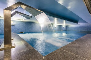 Uma piscina interior com design moderno, apresentando um elemento aquático único e uma parede revestida em azulejos azuis.