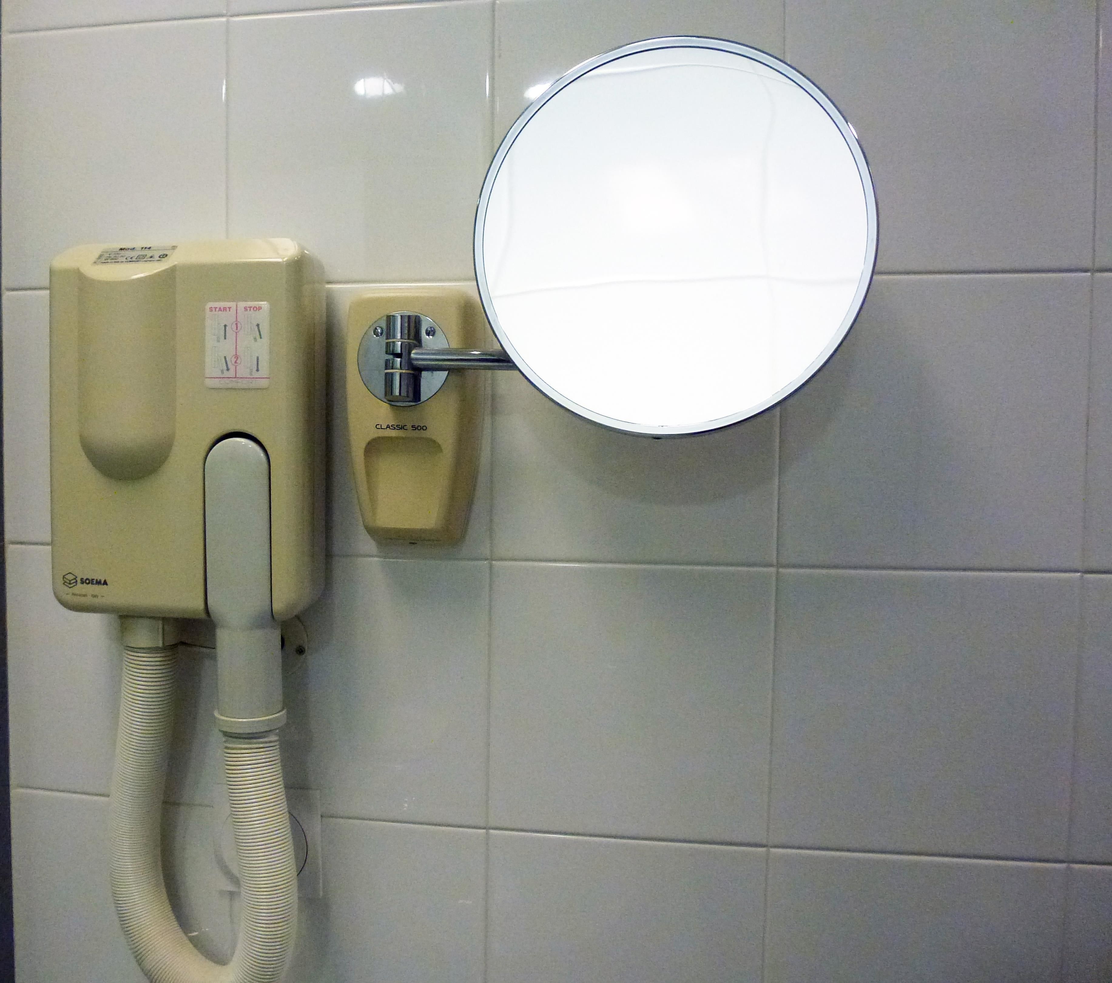 Sanitário com vaso sanitário fixado na parede, secador de mãos e espelho.