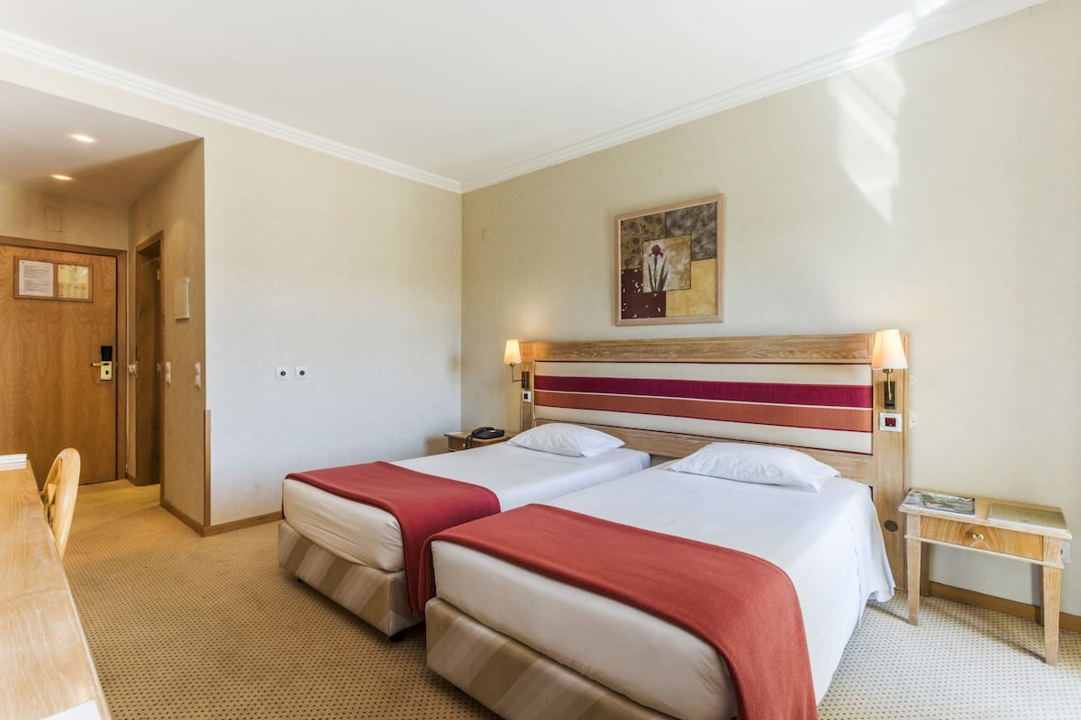 A hotel room with two beds, a wooden desk, and a small bedside table.