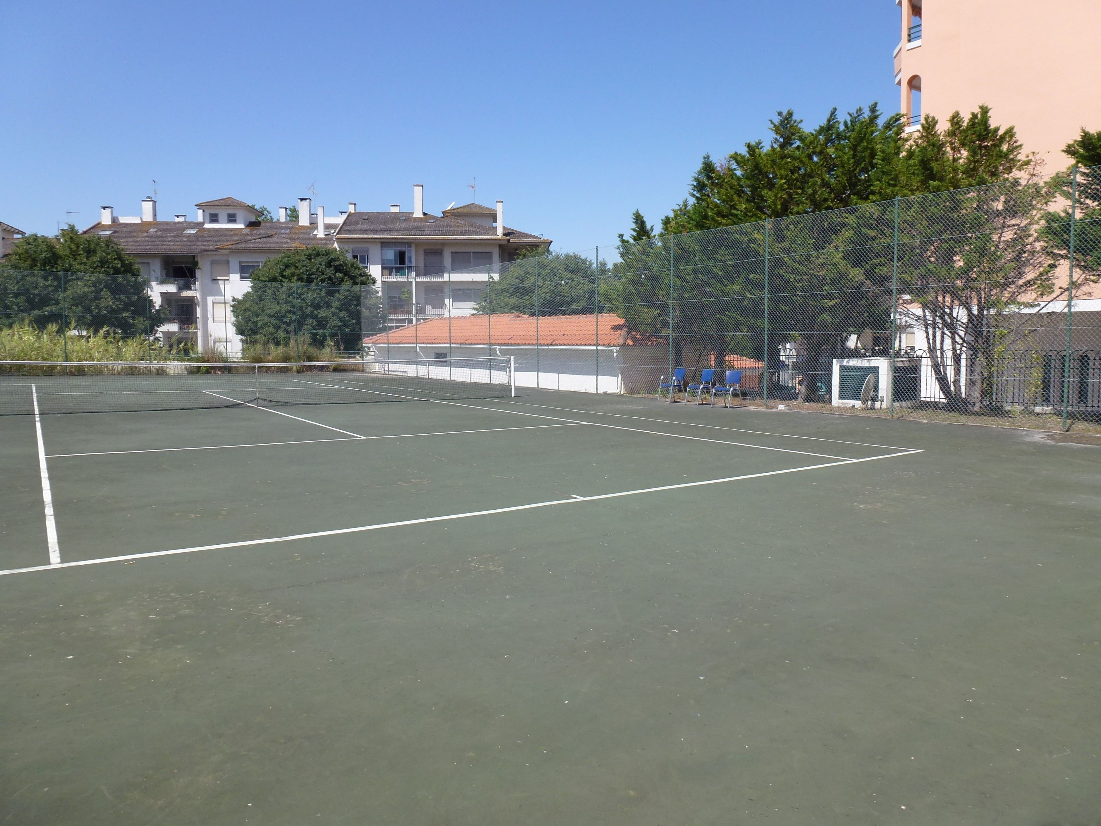 Un court de tennis en plein air, doté d’un filet, entouré d’une clôture et d’arbres.