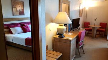 Habitación de hotel con cama, escritorio con lámpara, silla, mesita y televisor.