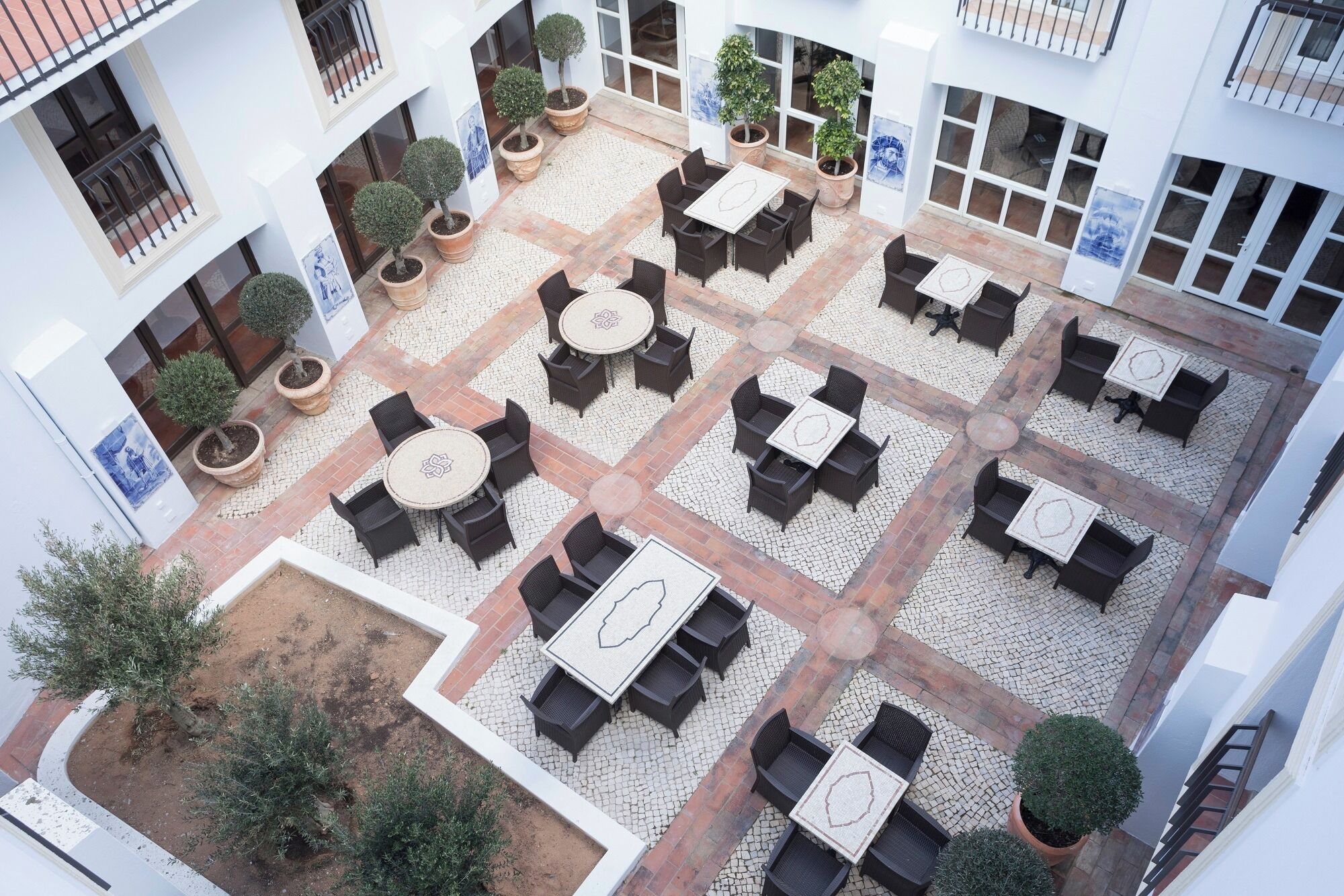 An outdoor patio area with multiple seating arrangements, surrounded by potted plants and a cobblestone floor.