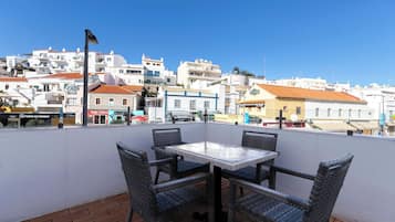 Una terraza con sillas de mimbre y una mesa, con vistas a un pueblo de edificios blancos y un cielo azul despejado.
