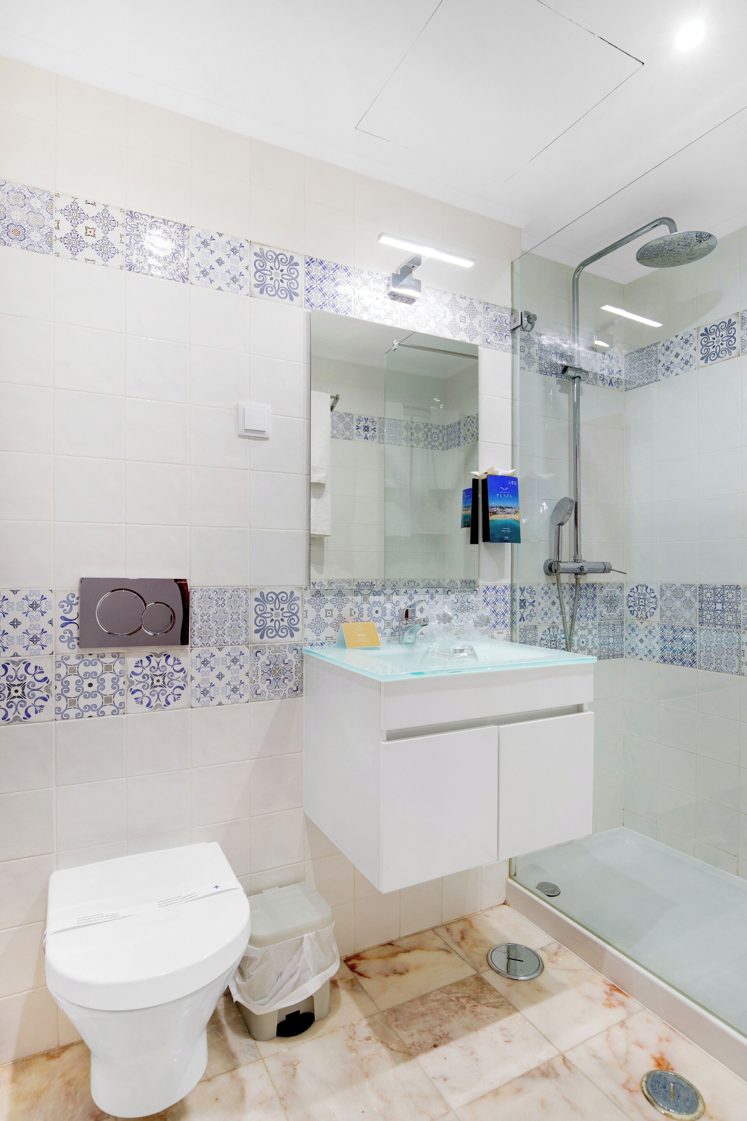 A bathroom with a toilet, a glass shower enclosure, a sink with a mirror, and patterned tiles on the walls.