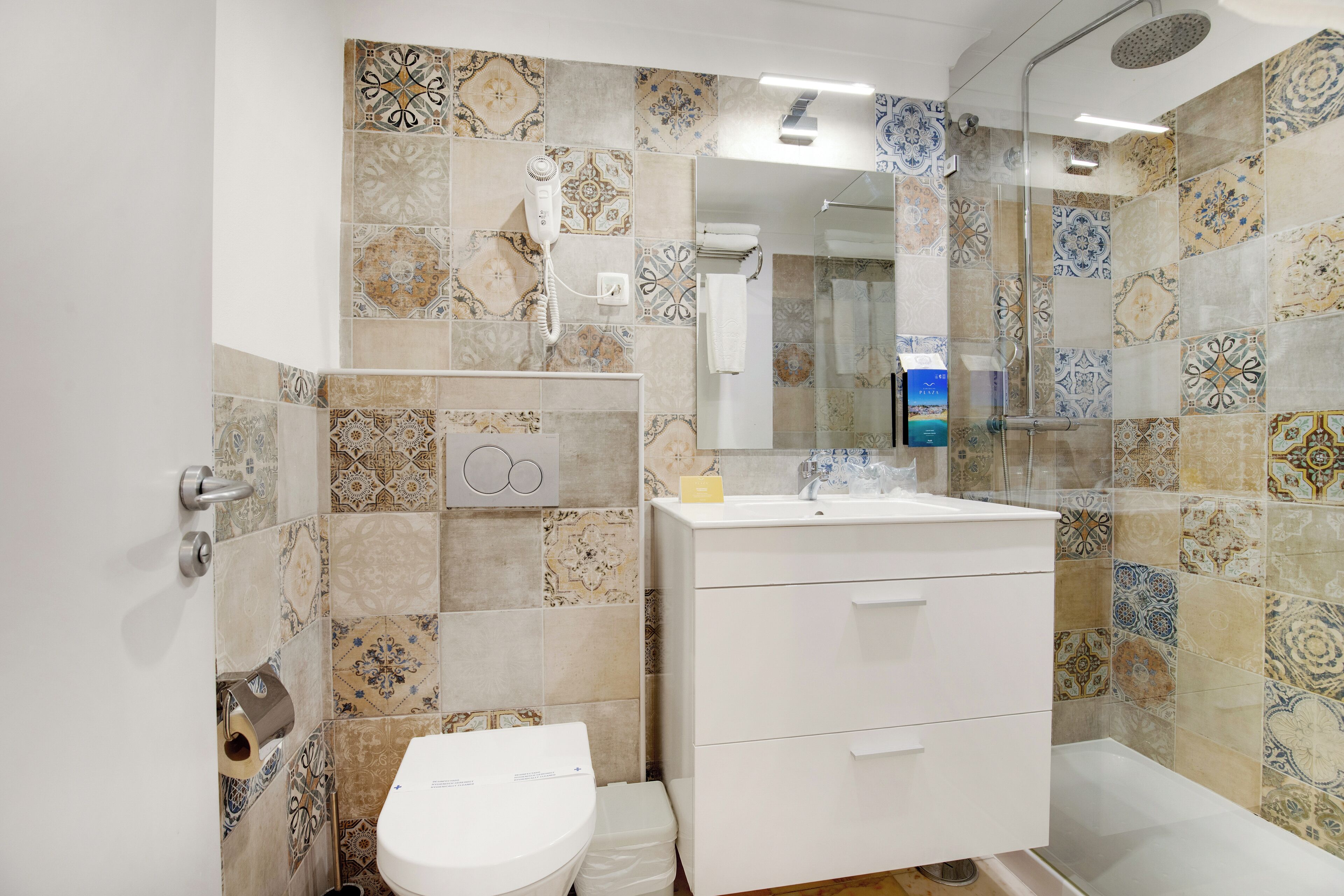 A bathroom with patterned tiles, a toilet, a sink, and a shower.