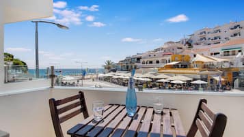 Une terrasse dotée de mobilier en bois, offrant une vue dégagée sur la plage et la mer, et bordée d’une rangée de restaurants avec des parasols.