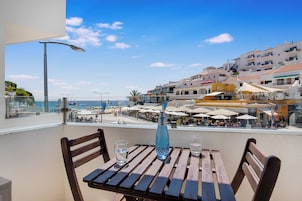 Una terraza con mobiliario de madera, vistas despejadas a la playa y al mar, y una hilera de restaurantes con sombrillas.