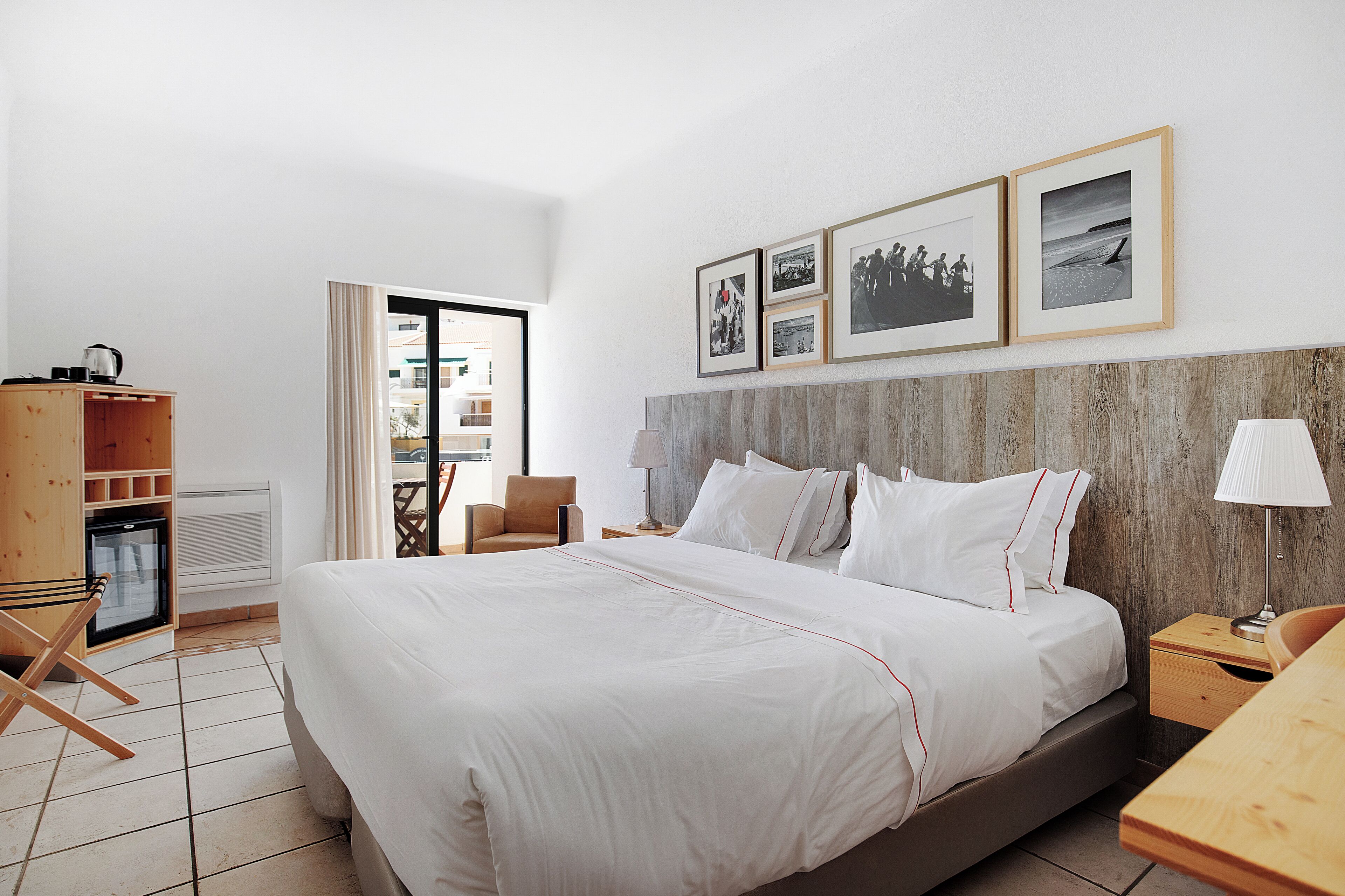 A hotel room with a large bed, a wooden headboard, a desk with a lamp, and a view of the outside.