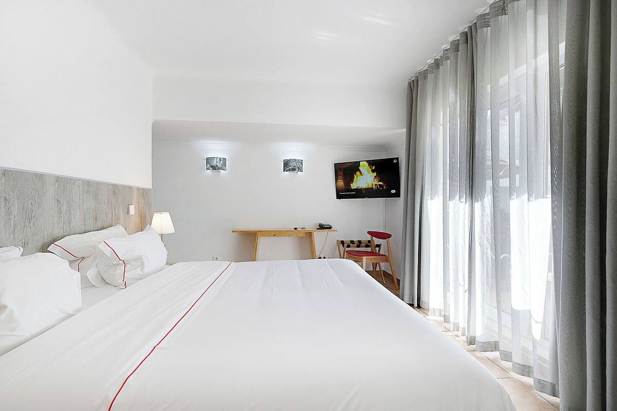 Una habitación de hotel con una cama grande, un escritorio, una silla, un televisor y una ventana con cortinas.