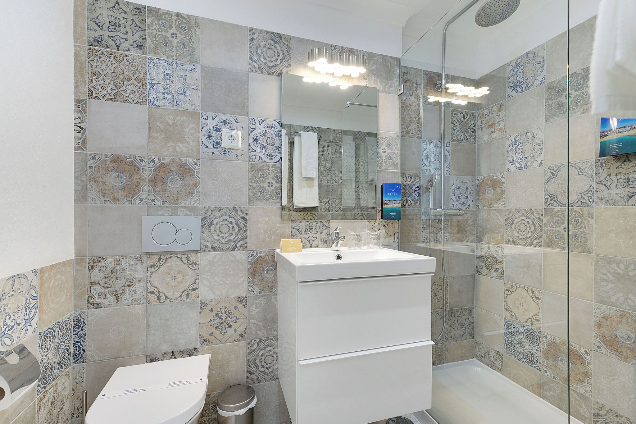 A bathroom with patterned tiles, a white sink, and a glass-enclosed shower.