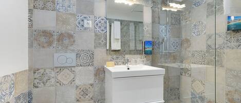 A bathroom with patterned tiles, a white sink, and a glass-enclosed shower.