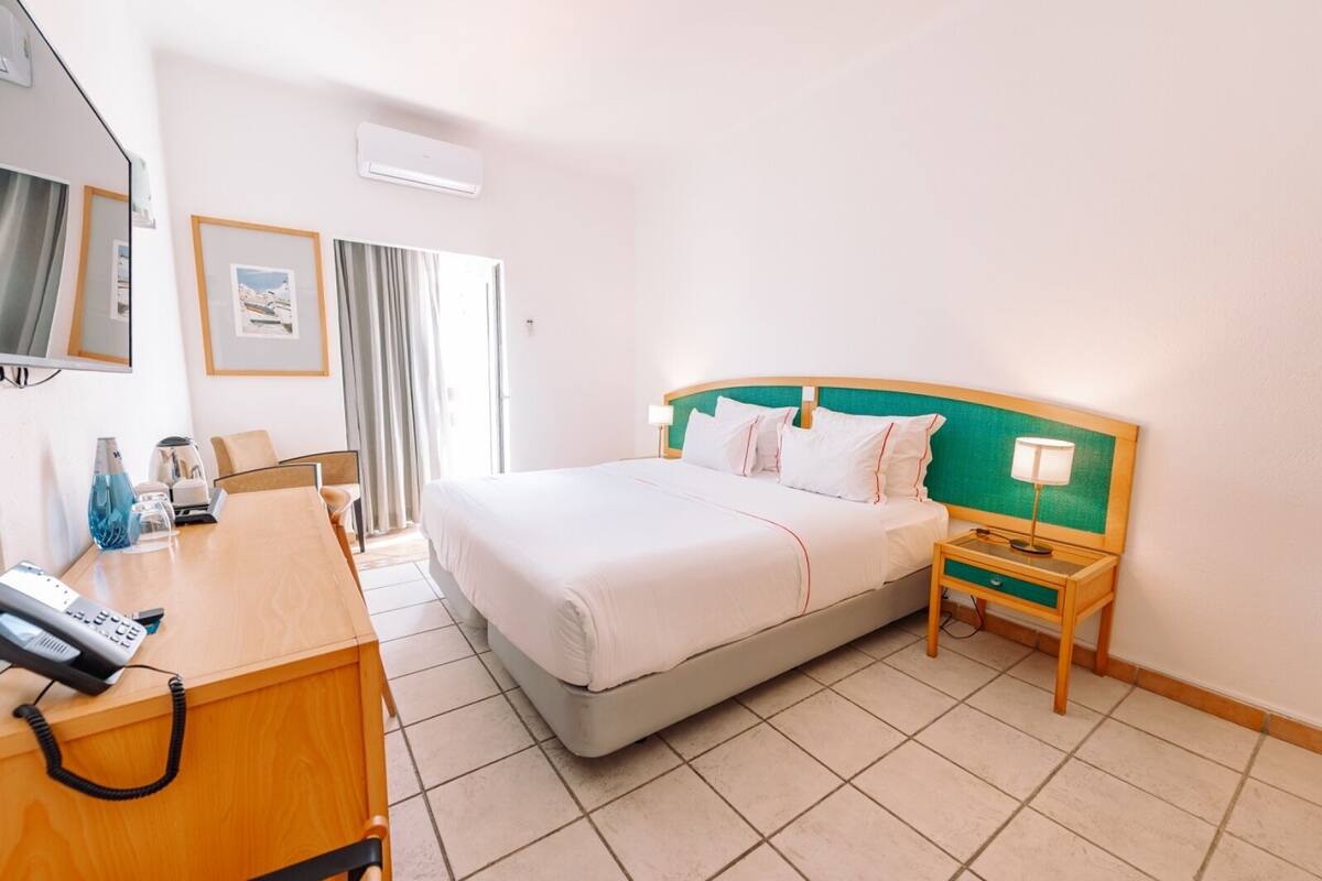 Una habitación de hotel con cama, mesita de noche, lámpara, escritorio con teléfono y televisión.
