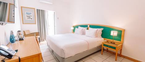 A hotel room with a bed, bedside table, lamp, desk with phone, and a TV.