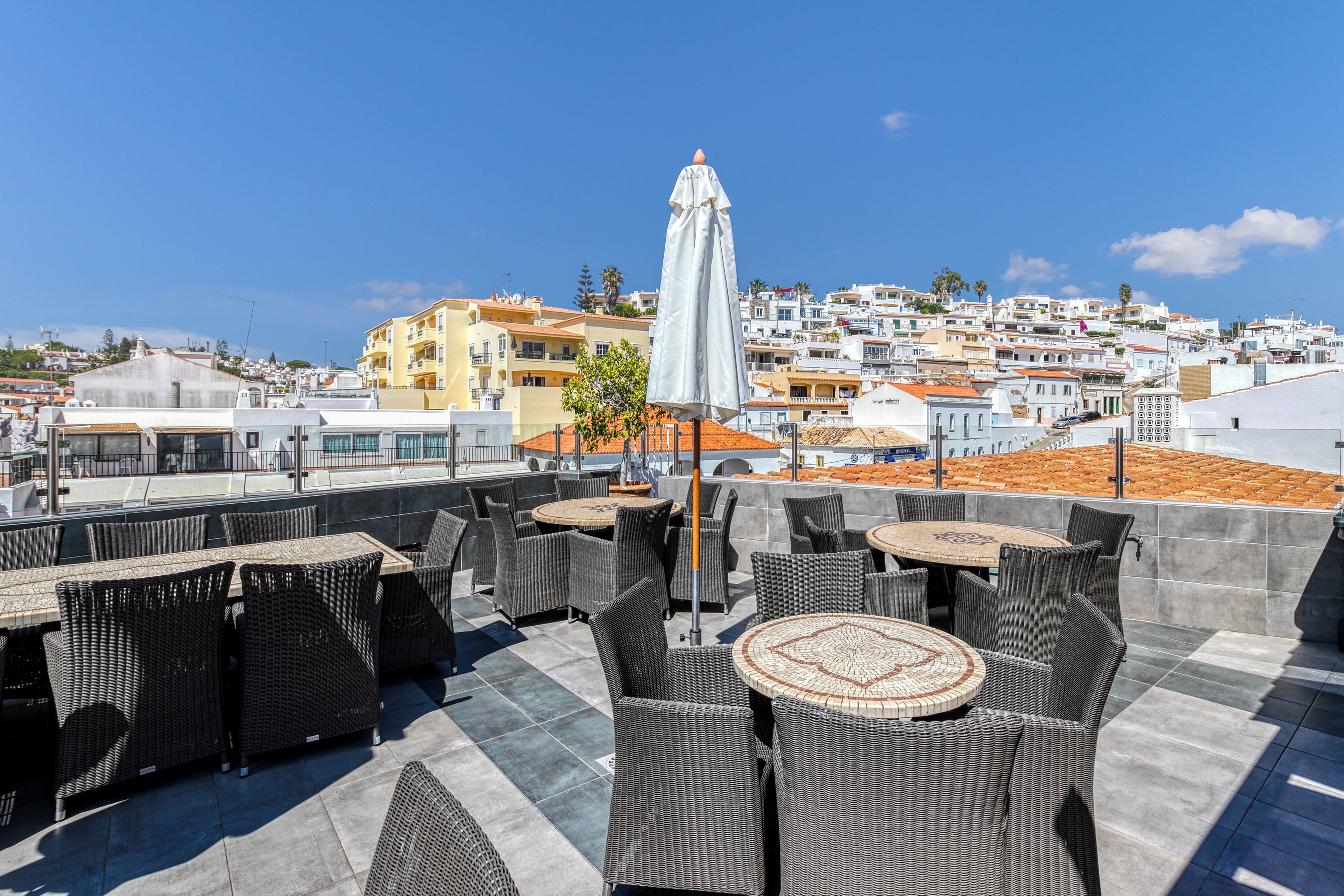 A rooftop terrace with wicker furniture and a view of a coastal town.