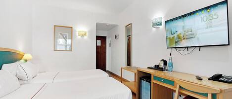 A hotel room with two beds, a desk, a television, and a small refrigerator.