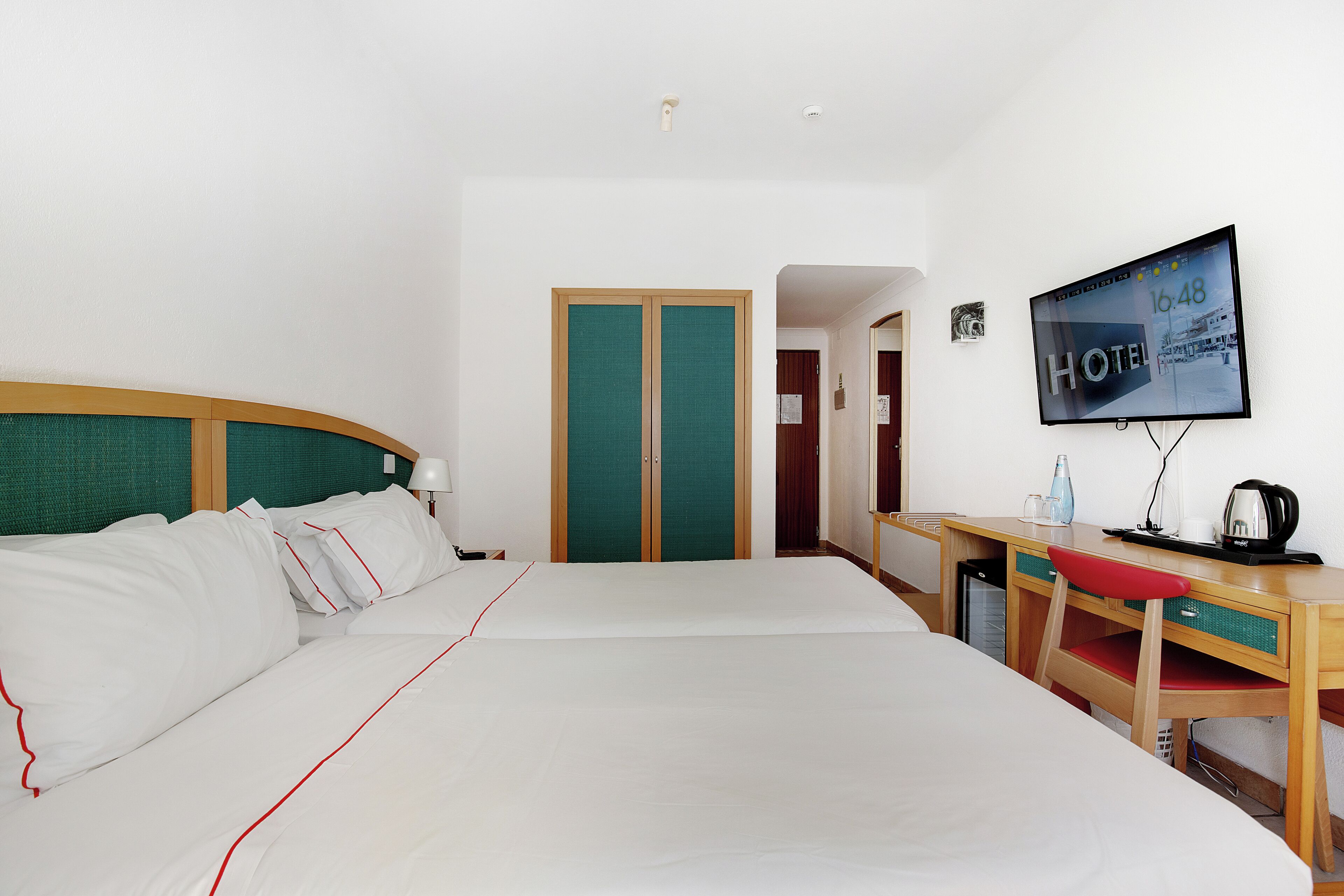 A hotel room with a bed, a desk, a television, and a wardrobe.