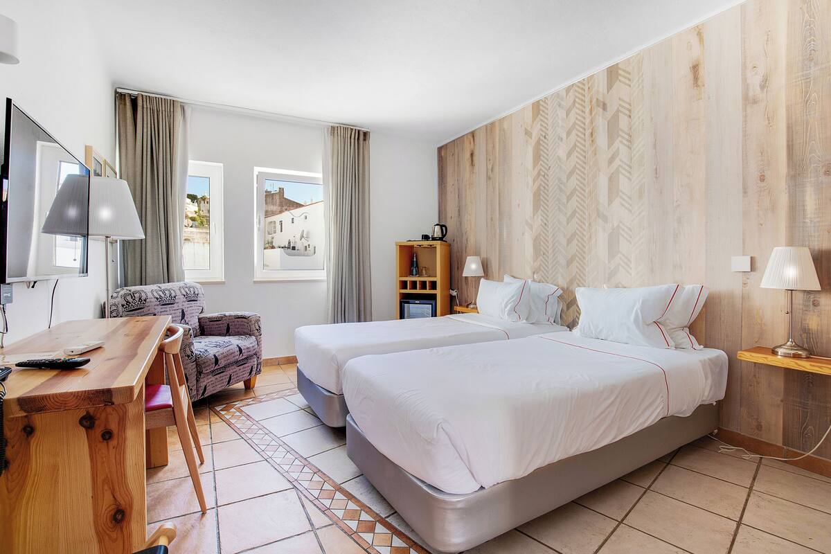 Habitación de hotel con dos camas, un escritorio, una silla, un televisor y vistas al exterior.