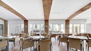 Een ruime eetruimte met hoge plafonds en zichtbare bakstenen muren, met meerdere tafels en stoelen voor diners.