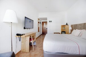 Habitación de hotel con cama, escritorio, silla, lámpara, televisión y un armario de madera.