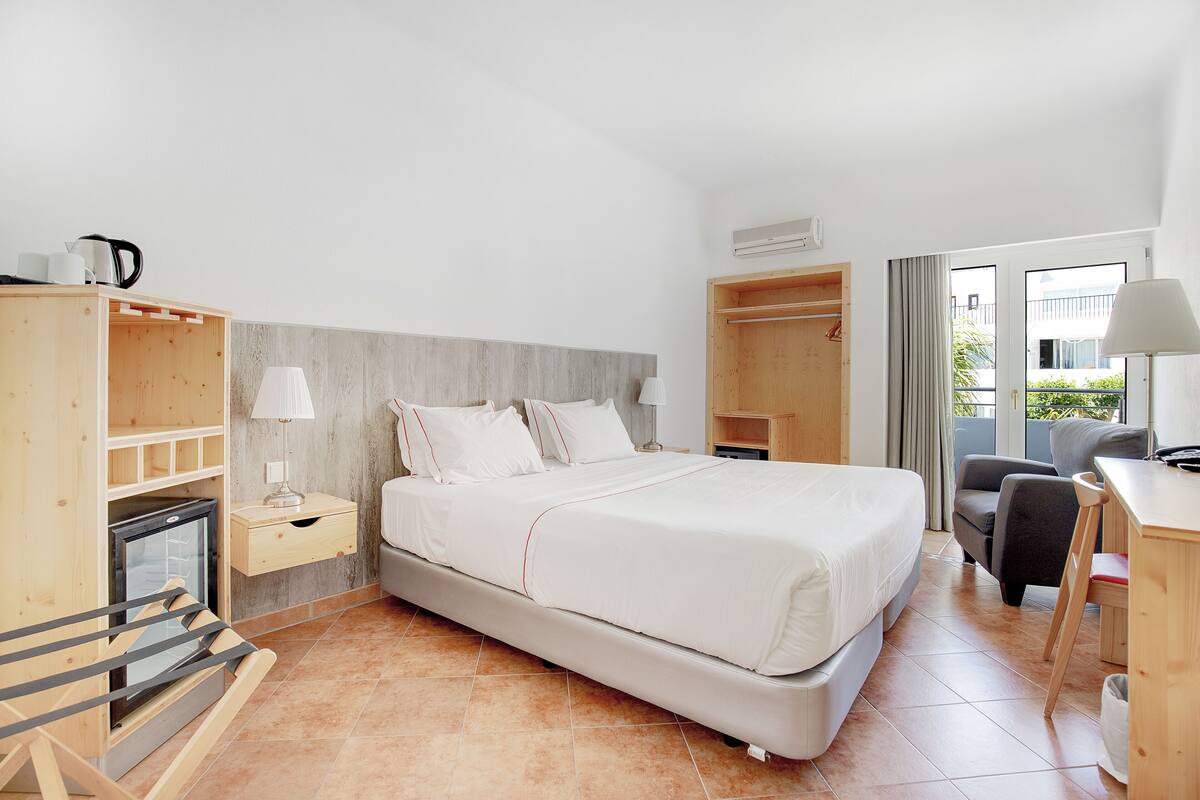 Una habitación de hotel con cama, escritorio, silla, armario y una pequeña kitchenette.