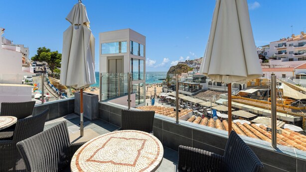 Een terras op het dak met rieten meubels, parasols en uitzicht op het strand en de oceaan.