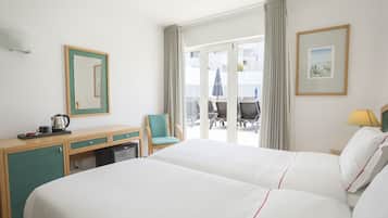 Habitación de hotel con cama, escritorio, silla, mesita con tetera y vistas al balcón exterior.