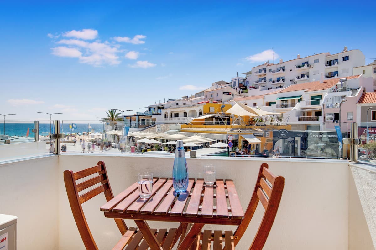 Una mesa de madera con dos sillas en un balcón con vistas a una playa y edificios.