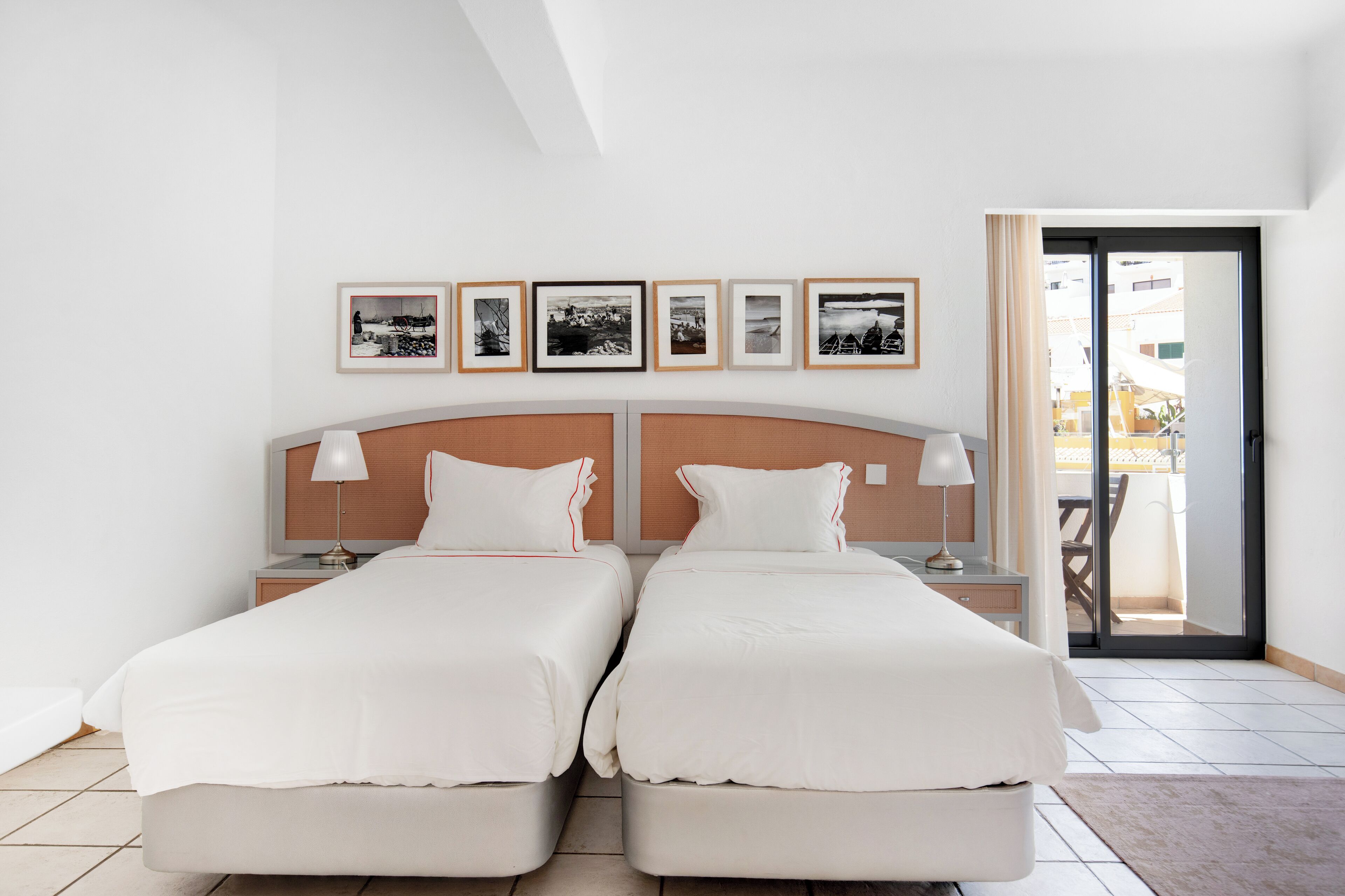 Une chambre double avec deux lits, une tête de lit en bois, des tables de chevet avec des lampes et un balcon avec vue.