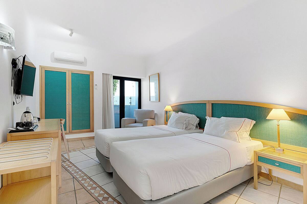 Habitación de hotel con dos camas, un escritorio, una silla, un televisor y una ventana con vistas.